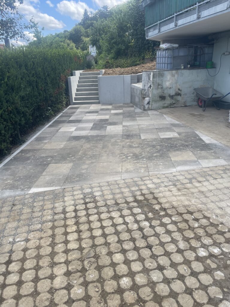 Newly paved stone patio with concrete stairs and a retaining wall in a garden.